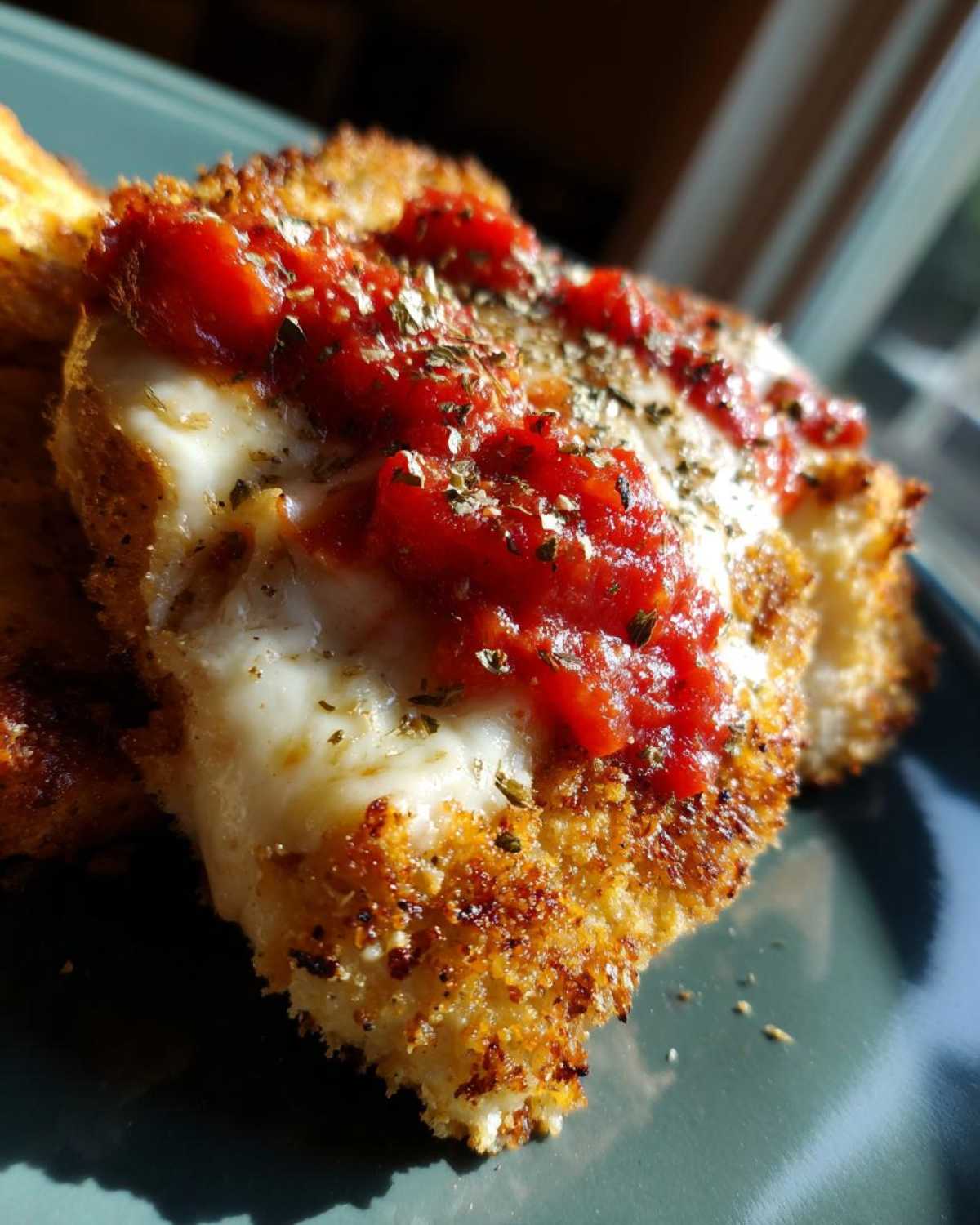 Close-up of a piece of Air Fryer Chicken Parmesan with melted mozzarella, marinara sauce, and dried herbs.
