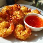 Plate of crispy, golden Air Fryer Coconut Shrimp served with a side of bright red sweet chili sauce.