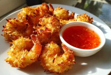 Plate of crispy, golden Air Fryer Coconut Shrimp served with a side of bright red sweet chili sauce.