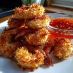 A pile of golden brown, crispy Air Fryer Coconut Shrimp served on a white plate next to a small bowl of sweet chili sauce.