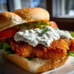 Close-up of an Air Fryer Crispy Fish Sandwich featuring a golden fried fillet topped with creamy tartar sauce and dill.