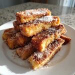 A stack of golden Air Fryer French Toast Sticks generously coated in cinnamon sugar on a white plate.