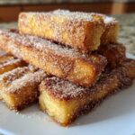A stack of golden Air Fryer French Toast Sticks generously coated in cinnamon sugar on a white plate.