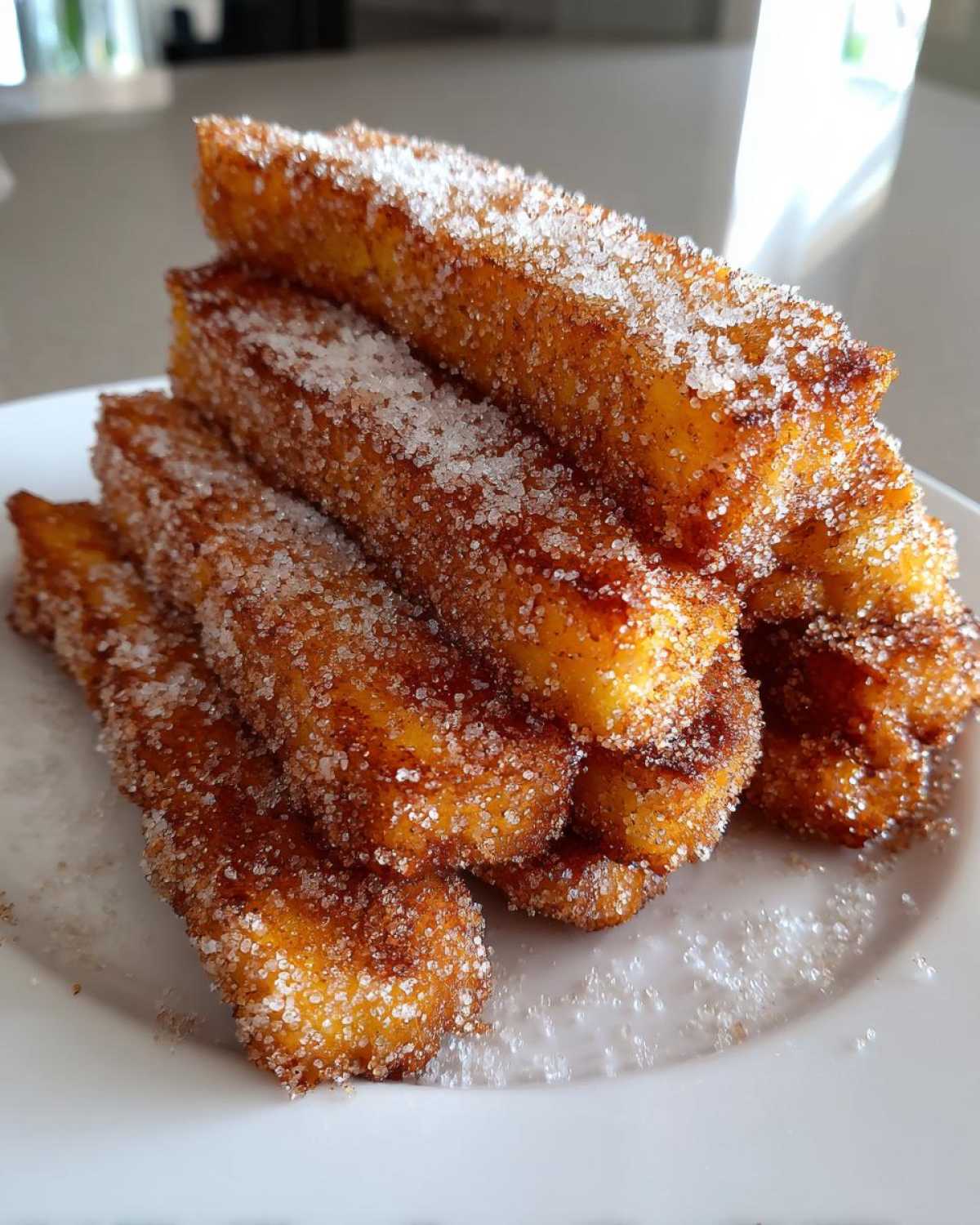 A stack of golden brown Air Fryer French Toast Sticks heavily coated in sparkling cinnamon sugar on a white plate.