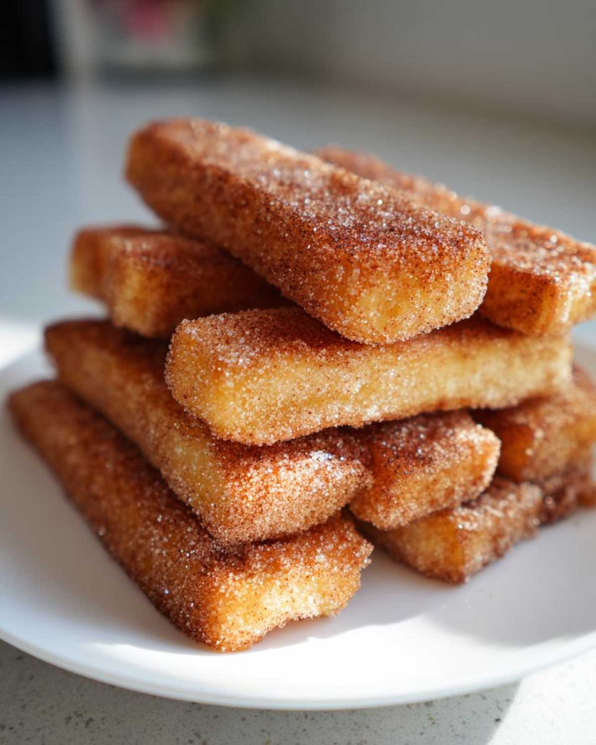 A close-up stack of golden Air Fryer French Toast Sticks generously coated in cinnamon sugar on a white plate.