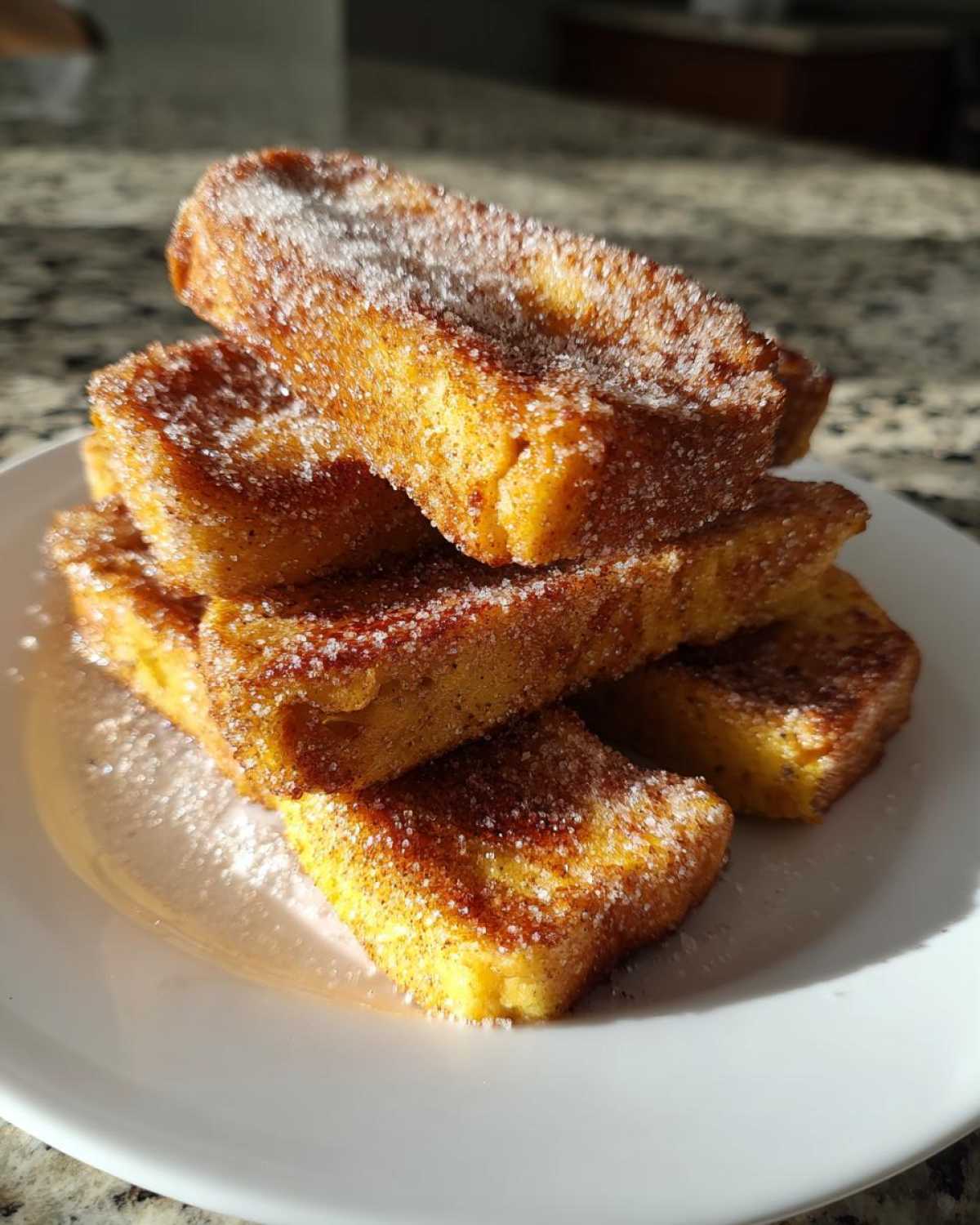A stack of golden brown Air Fryer French Toast Sticks generously coated in sparkling cinnamon sugar on a white plate.