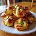 A close-up of several golden brown Air Fryer Garlic Knots, glistening with butter and topped with fresh parsley, piled on a white plate.