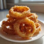 A close-up of crispy, golden Air Fryer Onion Rings stacked high on a small white plate.