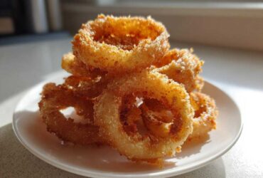 A close-up of crispy, golden Air Fryer Onion Rings stacked high on a small white plate.