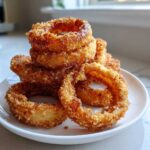 A close-up stack of crispy, golden brown Air Fryer Onion Rings served on a small white plate.