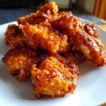 Close-up of crispy, glazed pieces of Air Fryer Orange Chicken piled on a white plate.