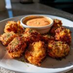 Plate of crispy, golden Air Fryer Salmon Bites garnished with parsley, served with a side of orange Bang Bang Sauce.