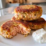 Close-up of golden brown Air Fryer Salmon Patties stacked on a white plate with a dollop of tartar sauce.