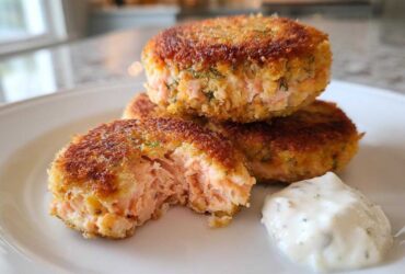 Close-up of golden brown Air Fryer Salmon Patties stacked on a white plate with a dollop of tartar sauce.