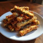 A pile of crispy, golden brown Air Fryer Zucchini Fries with Parmesan stacked on a white plate.