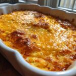 Close-up of hot, bubbly Baked Buffalo Chicken Dip topped with melted, golden-brown cheese in a white baking dish.