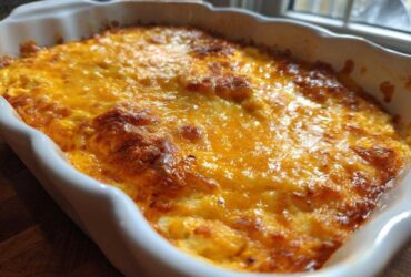 Close-up of hot, bubbly Baked Buffalo Chicken Dip topped with melted, golden-brown cheese in a white baking dish.