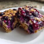 Close-up of two moist Blueberry Baked Oatmeal Squares featuring oats and rich, purple blueberry topping.