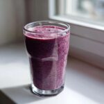 A thick, purple Blueberry Lemon Chia Smoothie speckled with chia seeds in a clear glass.