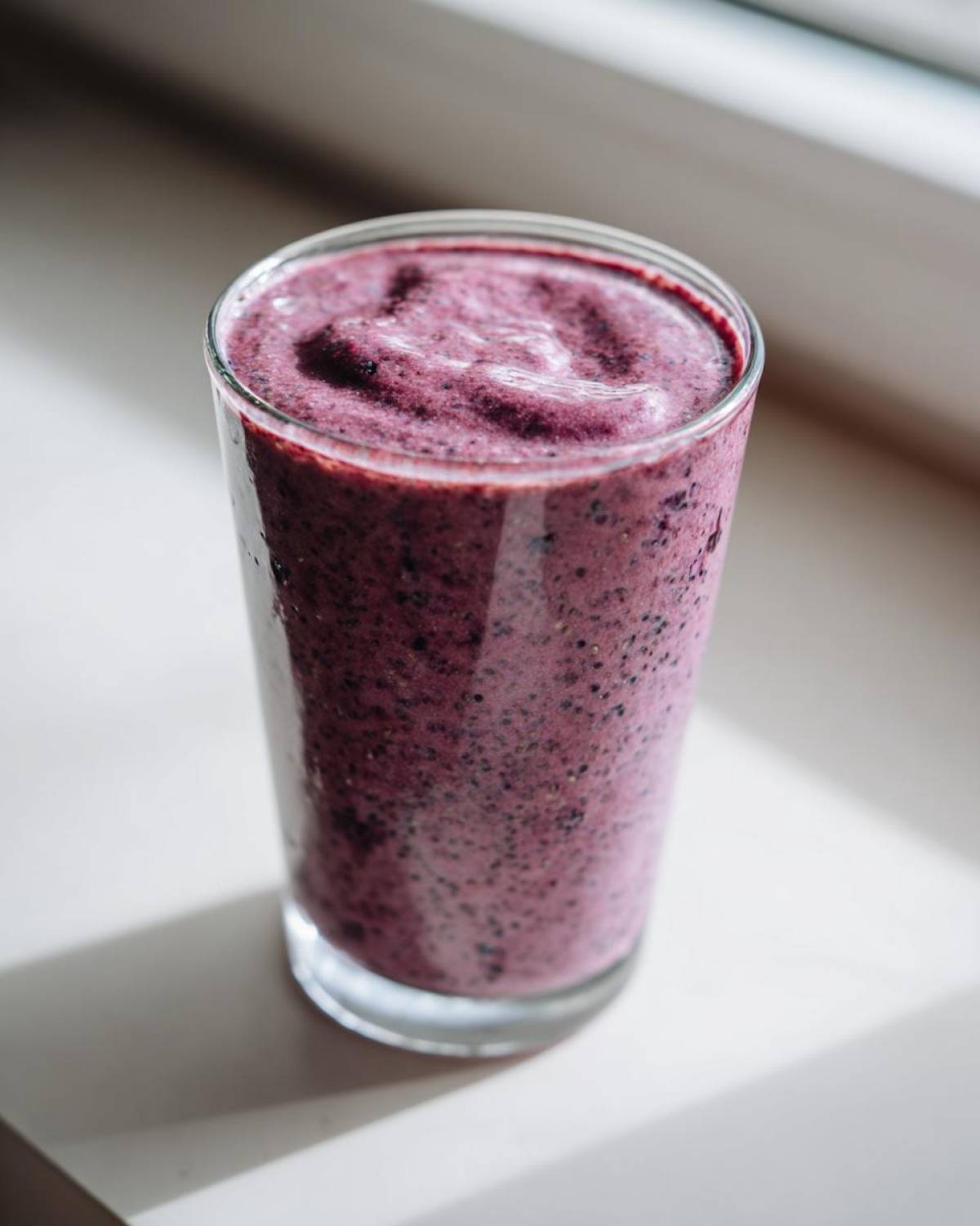 Close-up of a thick, purple Blueberry Lemon Chia Smoothie in a clear glass, showing visible chia seeds.