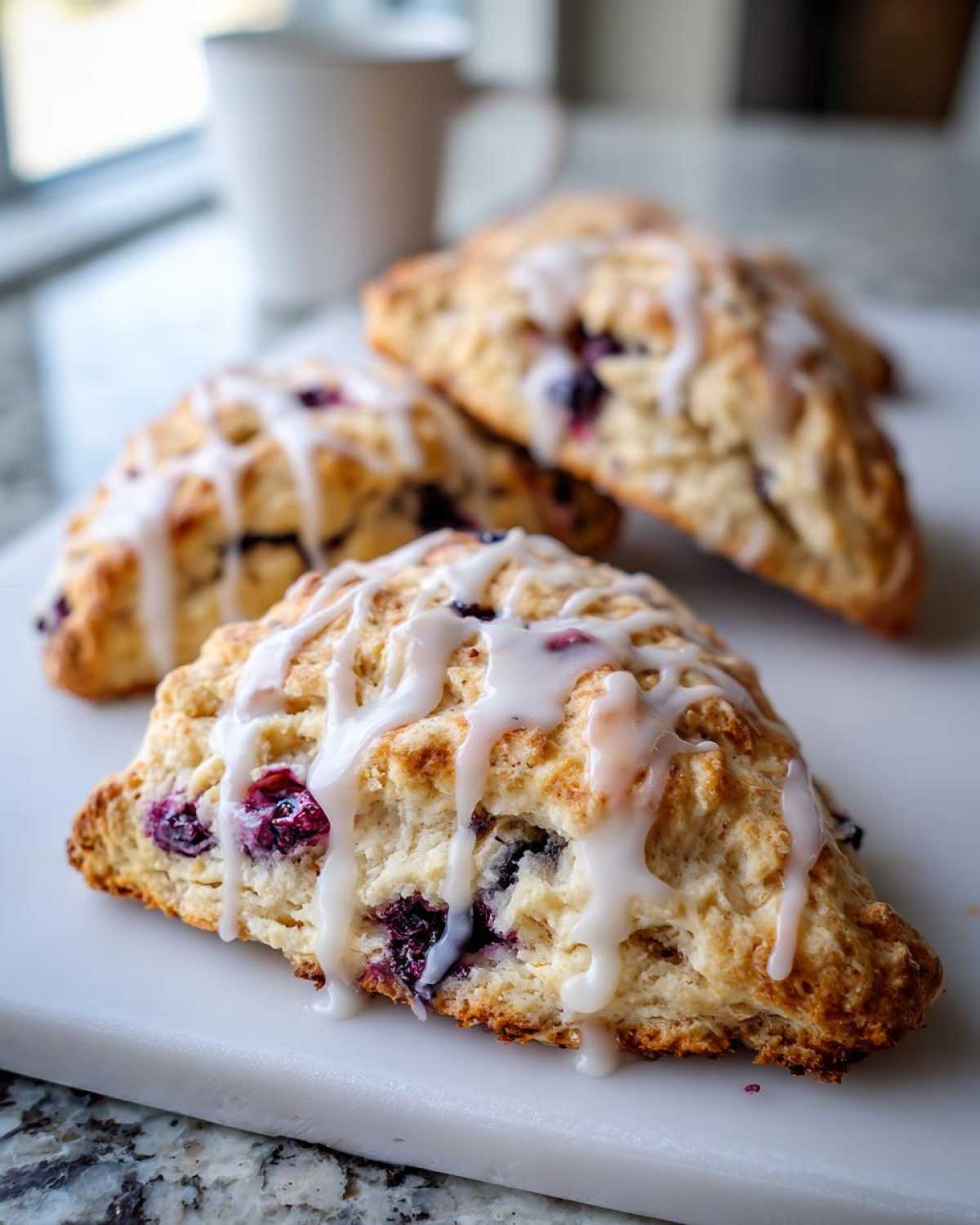 Close-up of freshly baked Blueberry Lemon Scones drizzled with a thick white glaze.