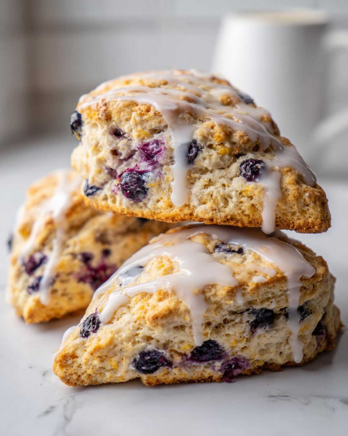 Three freshly baked Blueberry Lemon Scones stacked, drizzled with white lemon glaze.