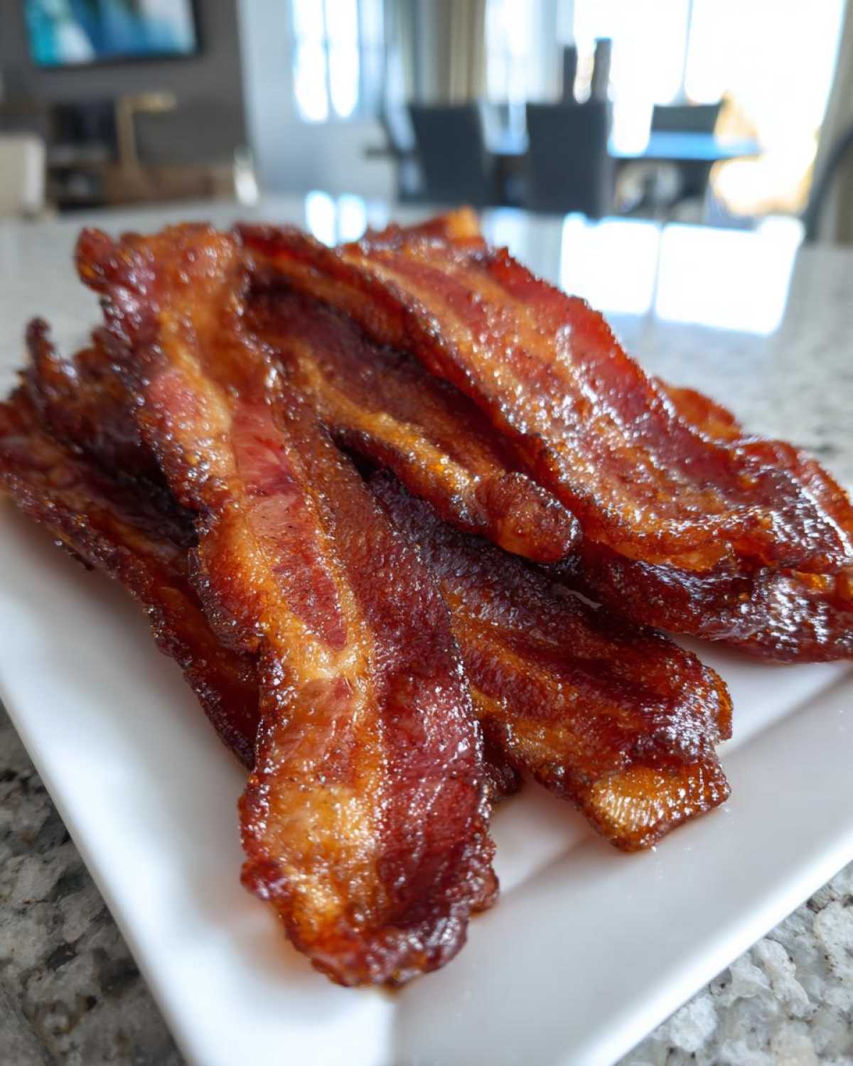 Close-up of perfectly cooked, shiny Brown Sugar Glazed Bacon strips piled on a white rectangular plate.