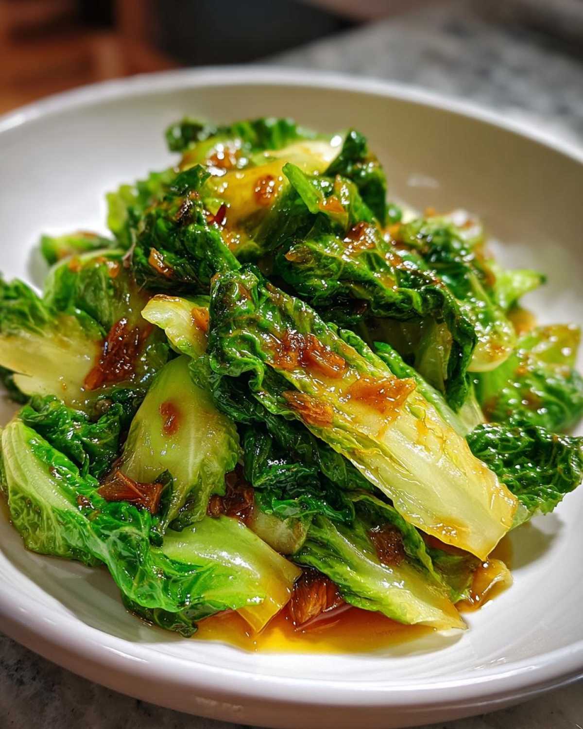 Close-up of vibrant green cabbage stir fry coated in a glossy garlic ginger sauce served in a white bowl.