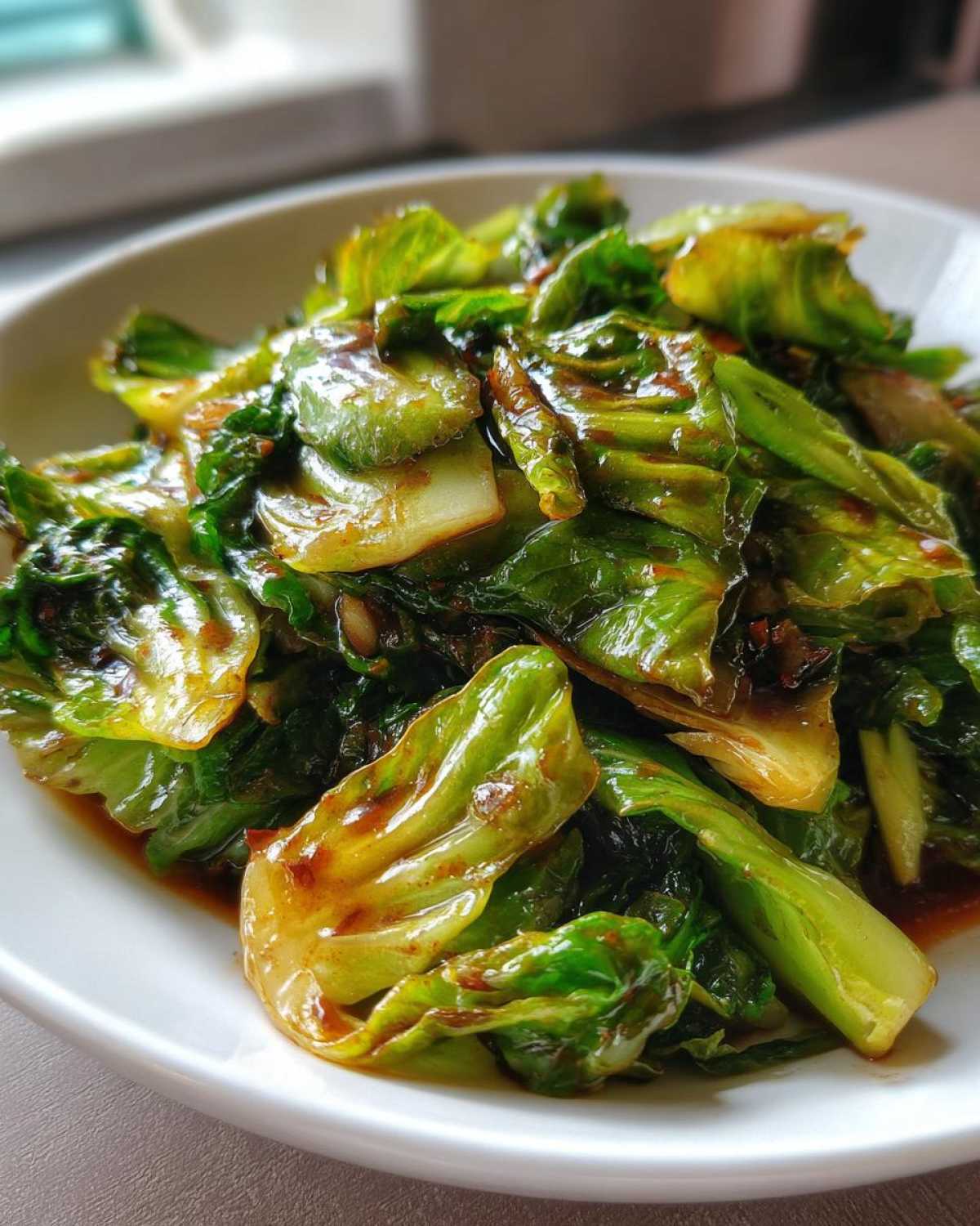 Close-up of vibrant green cabbage stir fry coated in a glossy garlic ginger sauce, served on a white plate.