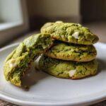 A stack of three chewy matcha white chocolate cookies, with one cookie broken open to show the soft interior.