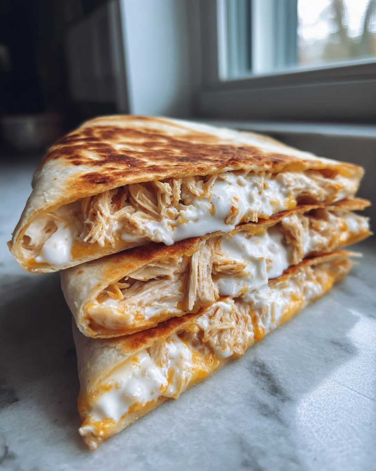 Three stacked wedges of a grilled chicken quesadilla generously filled with shredded chicken and creamy sauce.