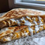 Close-up of a grilled chicken quesadilla cut in half, oozing melted cheese and drizzled with creamy Copycat Taco Bell Chicken Quesadilla Sauce.