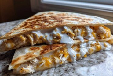 Close-up of a grilled chicken quesadilla cut in half, oozing melted cheese and drizzled with creamy Copycat Taco Bell Chicken Quesadilla Sauce.