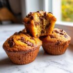 Close-up of three perfectly baked Chocolate Chip Banana Muffins, one split open showing the moist interior.