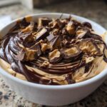 A white bowl filled with creamy Chocolate Peanut Butter Cheesecake Dip, drizzled with chocolate sauce and topped with chopped peanut butter cups.