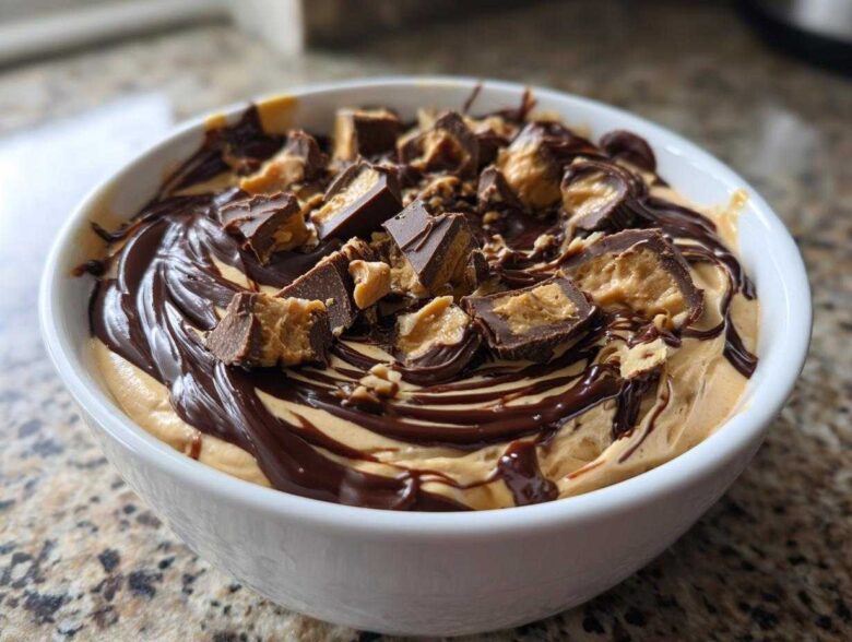 A white bowl filled with creamy Chocolate Peanut Butter Cheesecake Dip, drizzled with chocolate sauce and topped with chopped peanut butter cups.