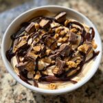 A close-up of rich Chocolate Peanut Butter Cheesecake Dip topped with chocolate syrup and chopped peanut butter cups.
