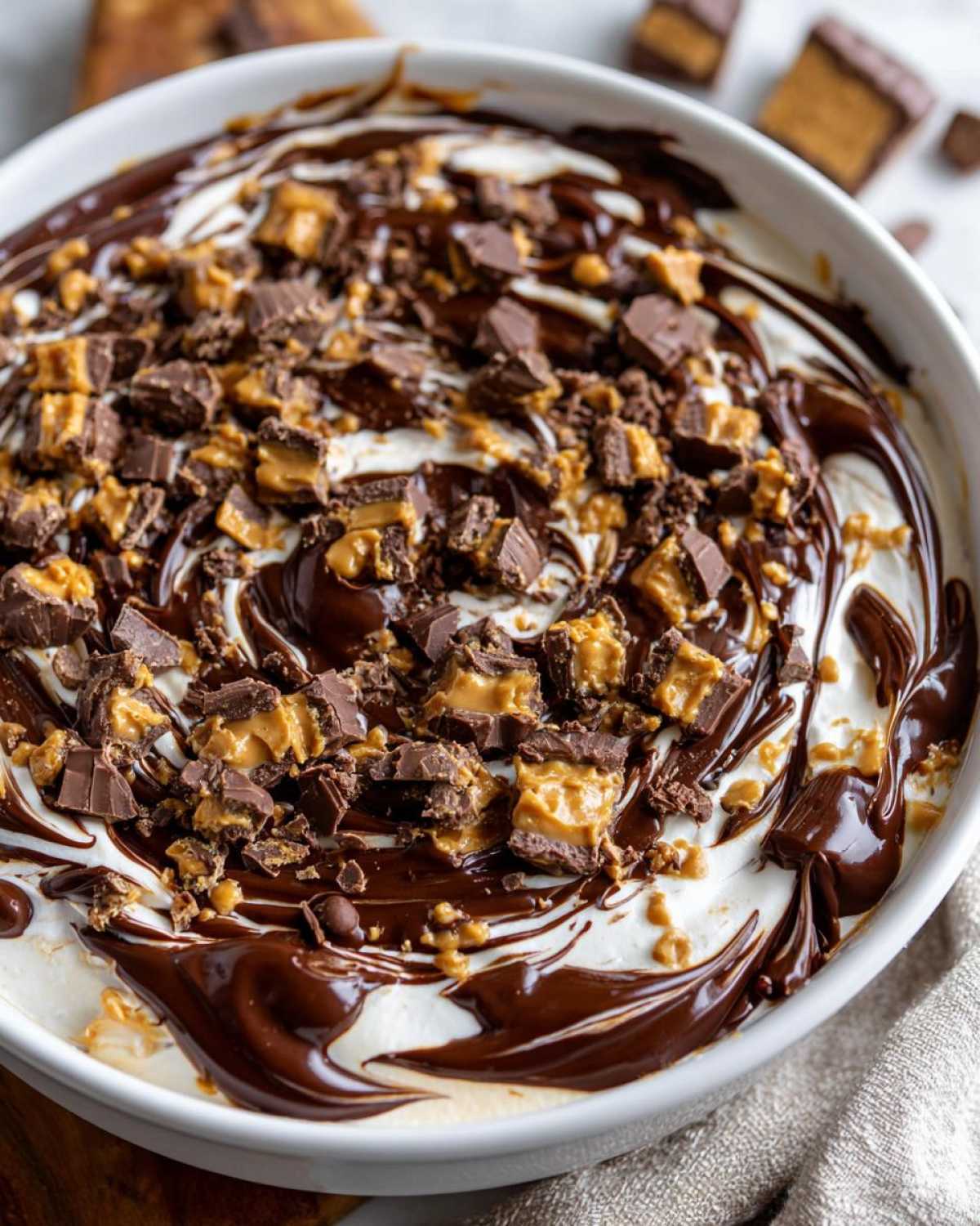 Close-up of Chocolate Peanut Butter Cheesecake Dip swirled with fudge and topped with chopped peanut butter cups.