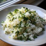 A close-up of fluffy Cilantro Lime Rice topped with fresh green herbs and bright yellow lime zest in a white bowl.