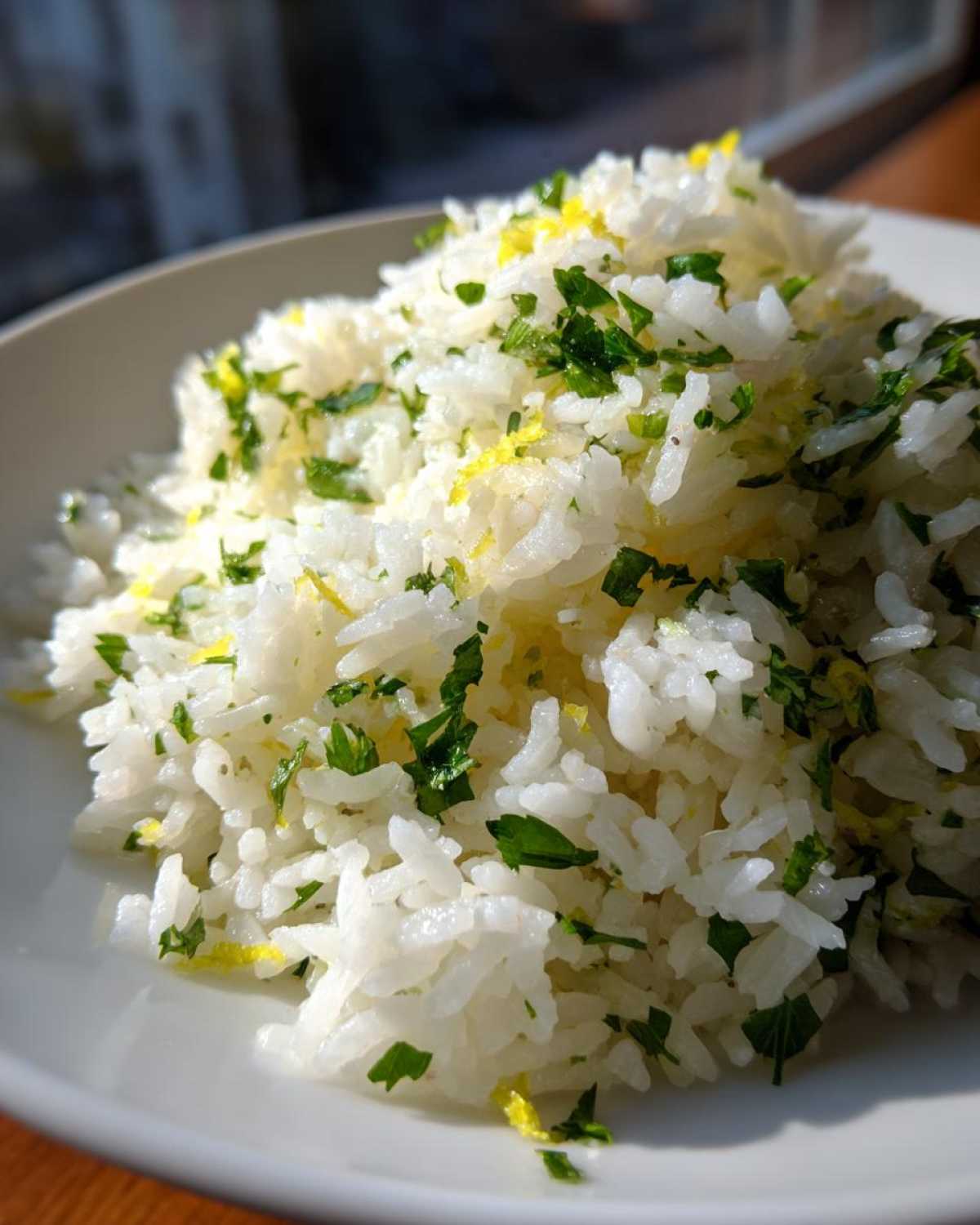 Close-up of fluffy Cilantro Lime Rice topped with chopped cilantro and bright yellow lime zest on a white plate.