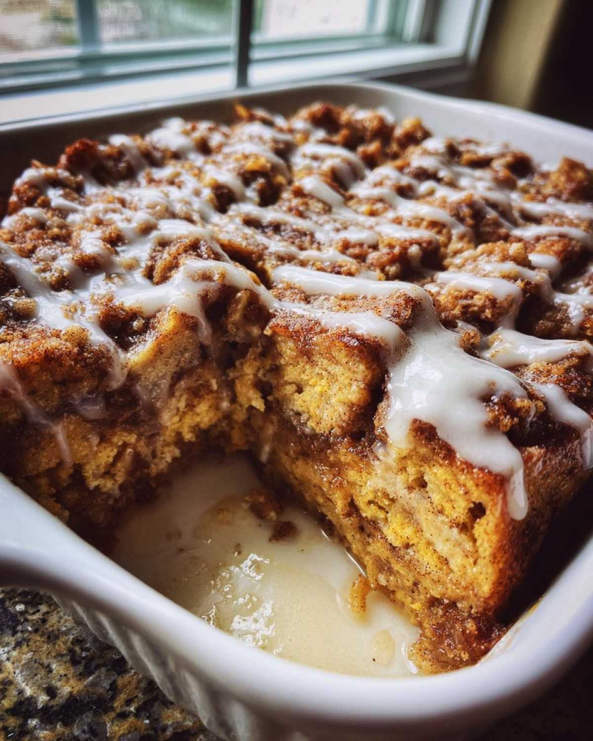 A close-up of a serving removed from the Cinnamon Roll Overnight French Toast Bake, drizzled with icing.