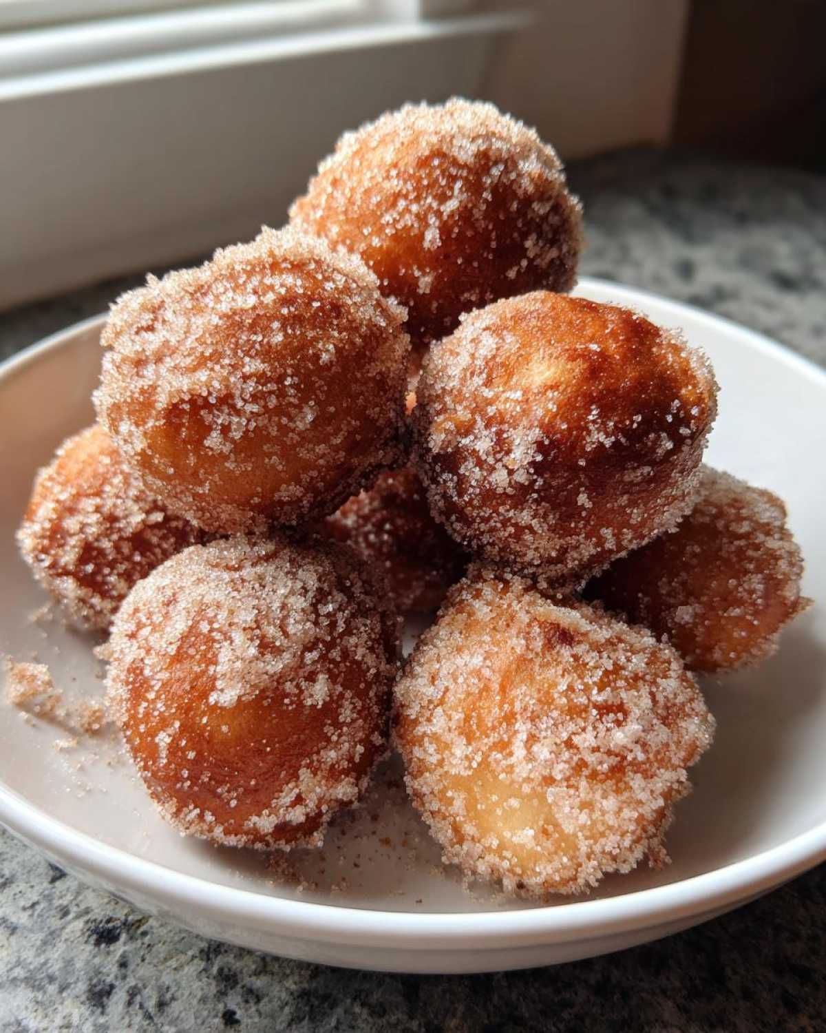 A close-up shot of several golden brown Cinnamon Sugar Air Fryer Donuts piled high in a white bowl.