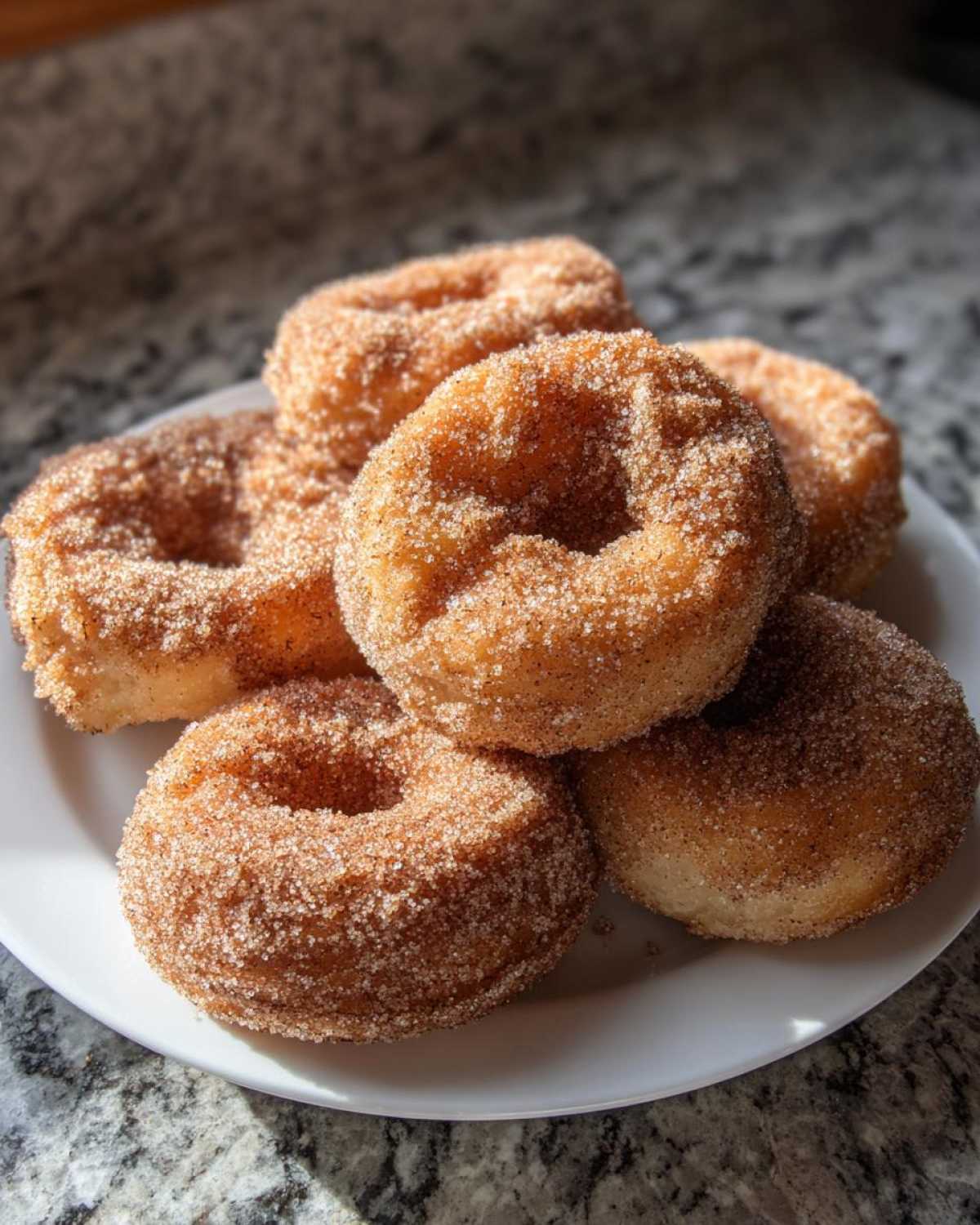 A stack of freshly made Cinnamon Sugar Air Fryer Donuts generously coated in sparkling cinnamon sugar.
