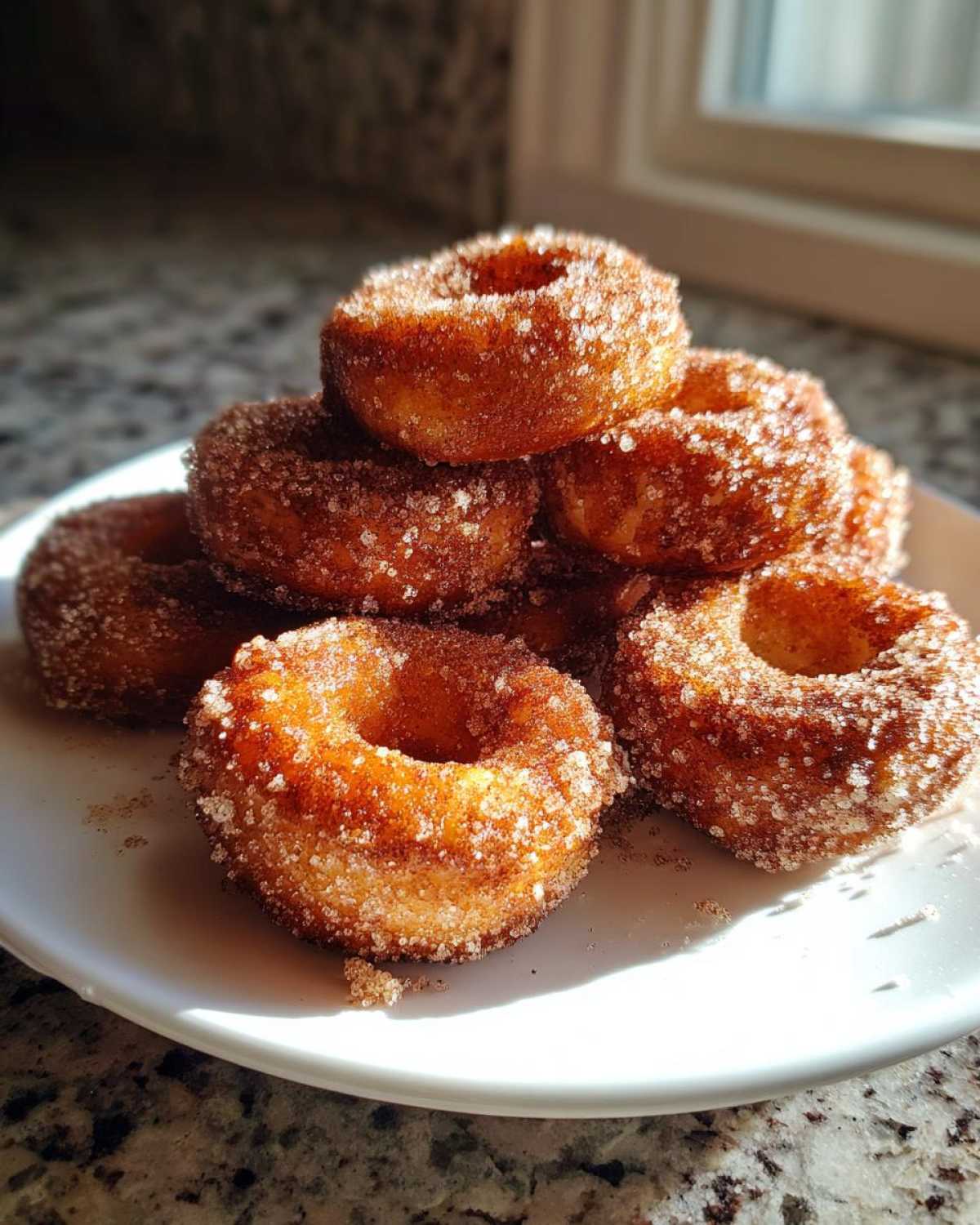 A stack of golden brown Cinnamon Sugar Air Fryer Donuts heavily coated in sparkling sugar crystals, resting on a white plate.
