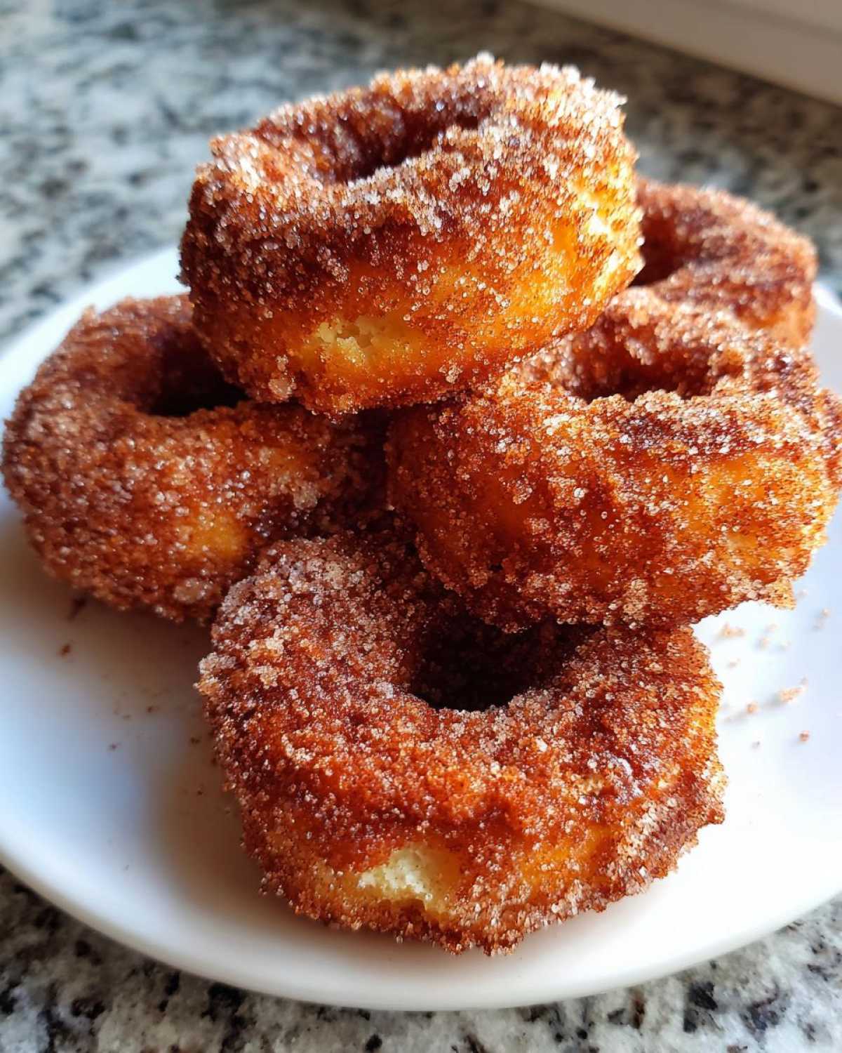A close-up stack of golden brown Cinnamon Sugar Air Fryer Donuts heavily coated in sparkling cinnamon sugar.