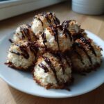 A plate piled high with golden-edged Coconut Macaroons with Dark Chocolate Drizzle, catching the sunlight.