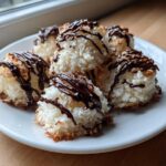 Close-up of several golden-edged Coconut Macaroons with Dark Chocolate Drizzle stacked on a white plate.