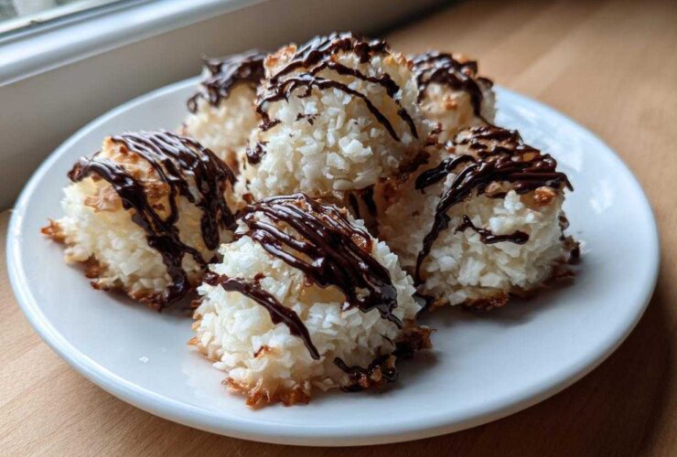 Close-up of several golden-edged Coconut Macaroons with Dark Chocolate Drizzle stacked on a white plate.