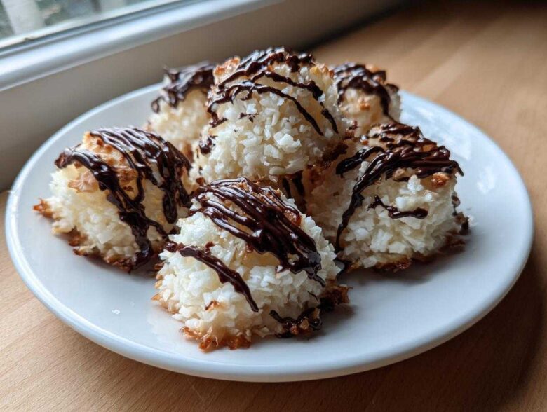 Close-up of several golden-edged Coconut Macaroons with Dark Chocolate Drizzle stacked on a white plate.