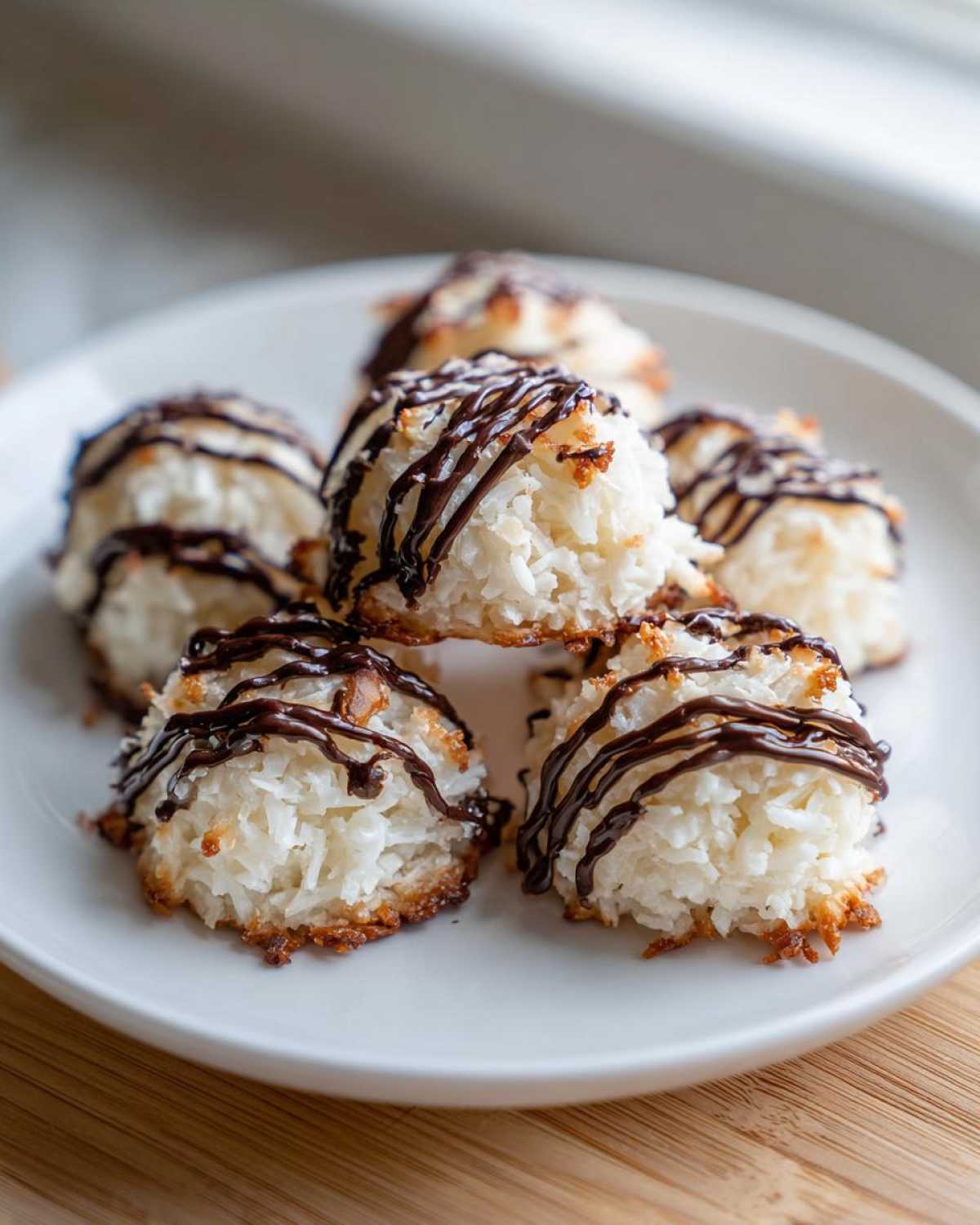 A stack of freshly baked Coconut Macaroons with Dark Chocolate Drizzle resting on a white plate.